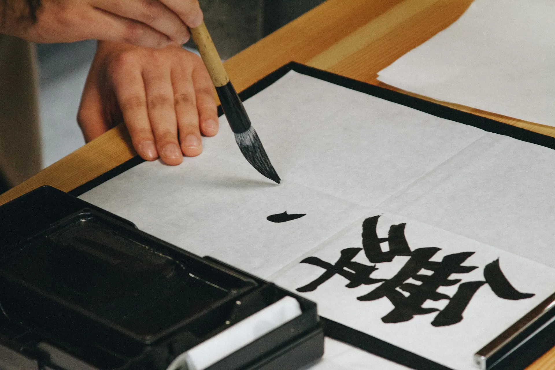 Person holding black paint brush while painting black text on white paper