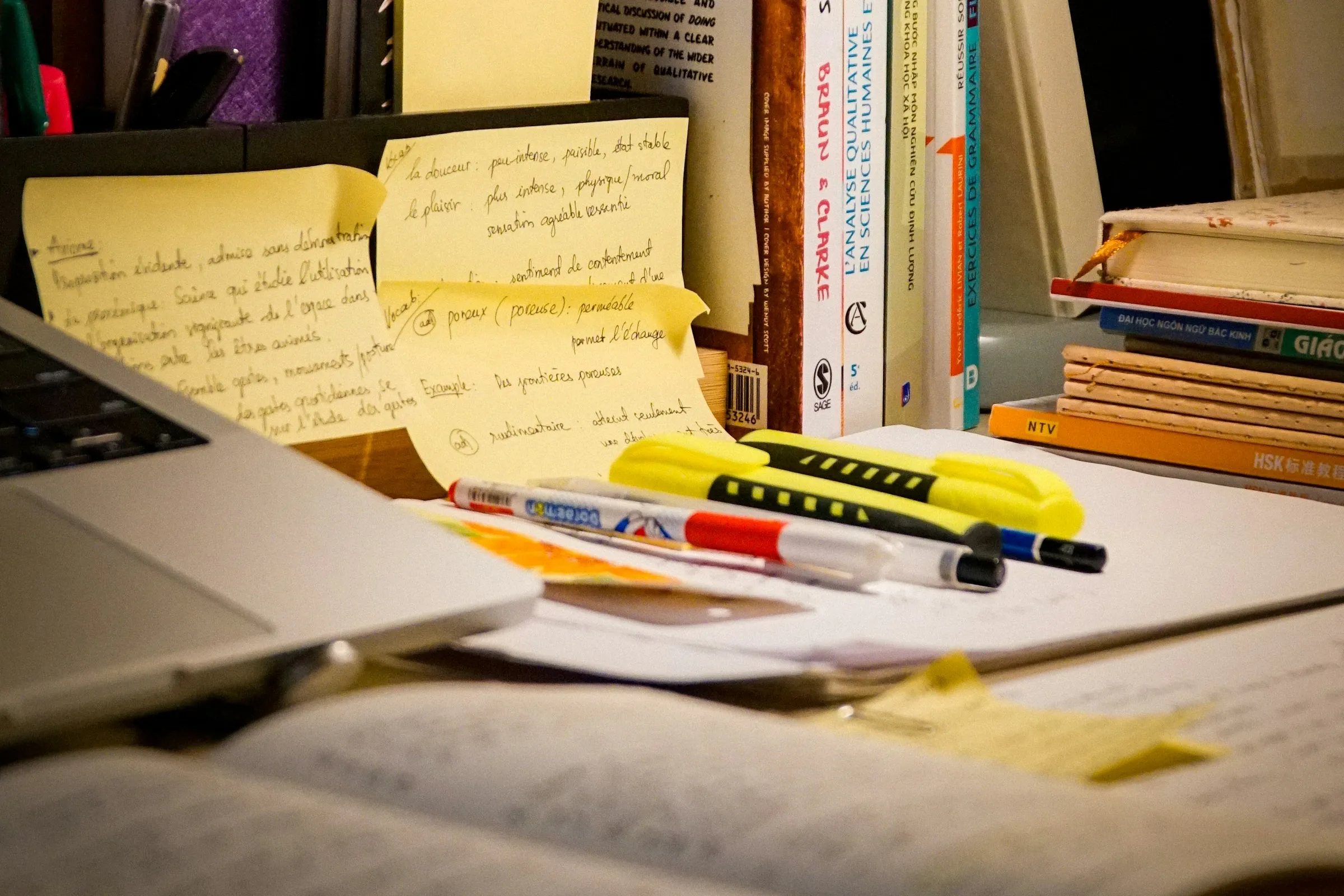 A study desk at night, with handwritten sticky notes, highlighters, books and an open laptop
