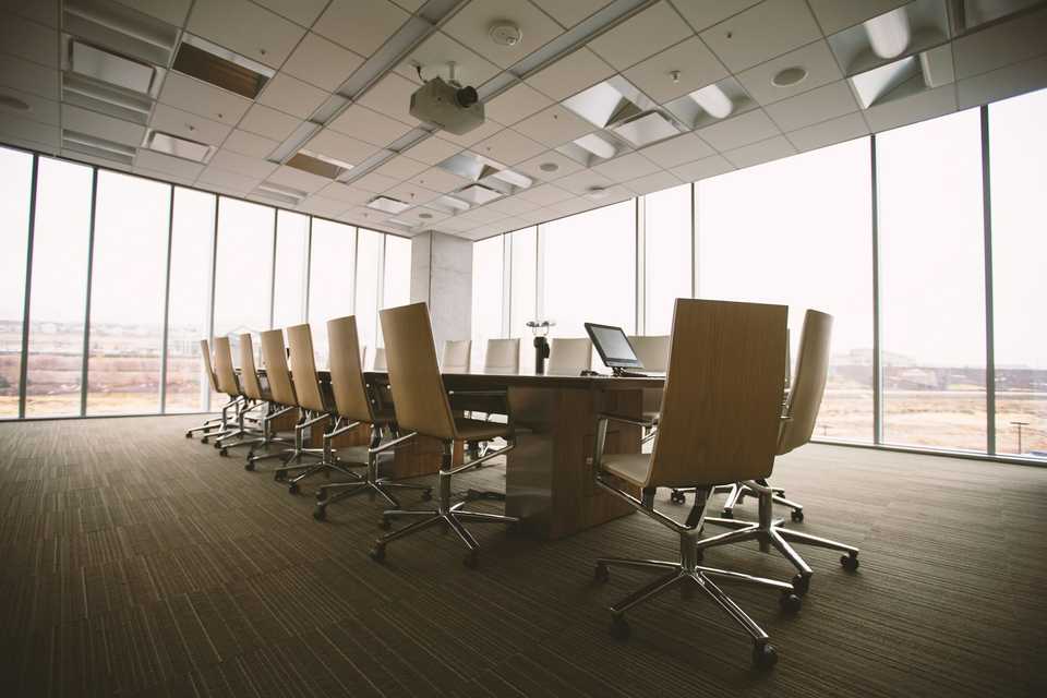 Empty conference room, with chairs around a long table and a single open laptop