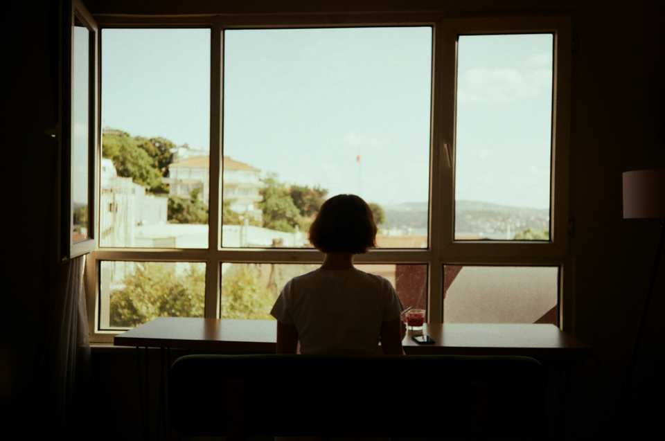 A person seen from behind, sitting at a table and looking out a large window over the city