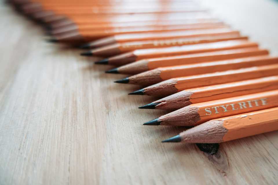 A row of freshly sharpened orange pencils on a wooden table